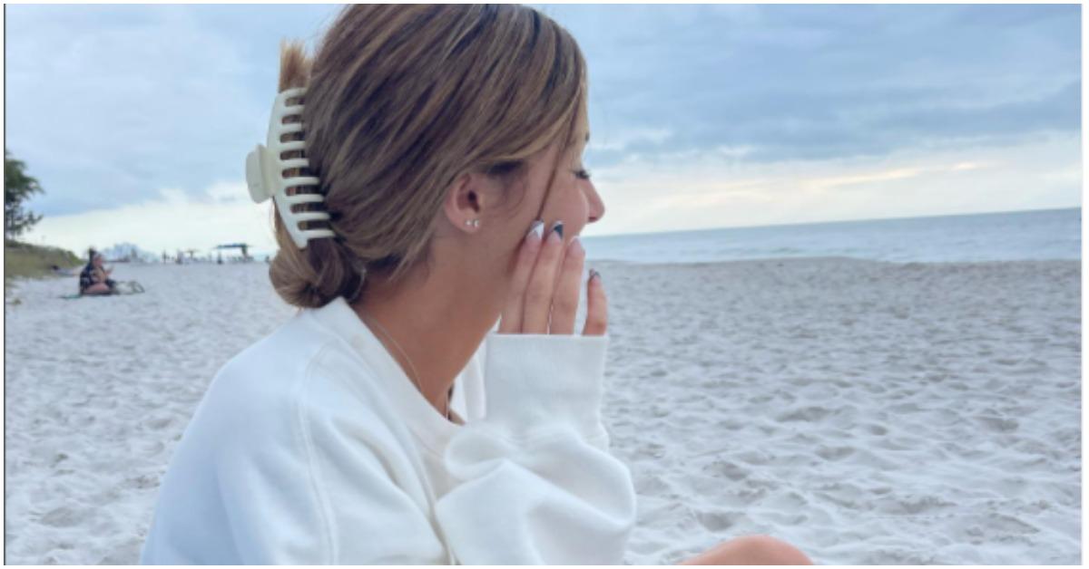 Ava Majury sitting down at the beach in a white sweatshirt. 