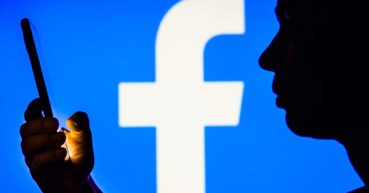 In this photo illustration, a woman's silhouette holds a smartphone with the Facebook logo in the background