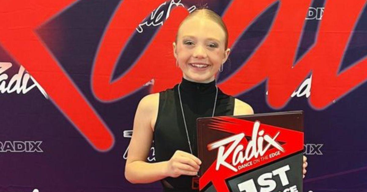 Everleigh Rose poses at a dance competition, showing off an award