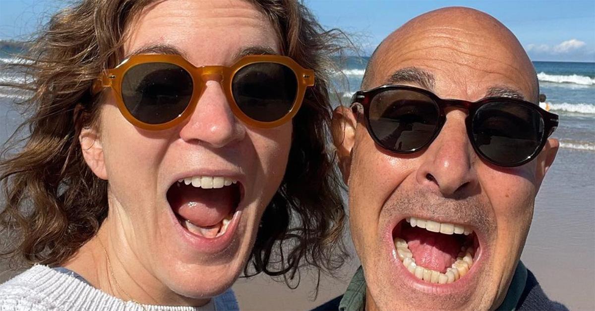 Stanley Tucci and Felicity Blunt on the beach with their mouths open. 