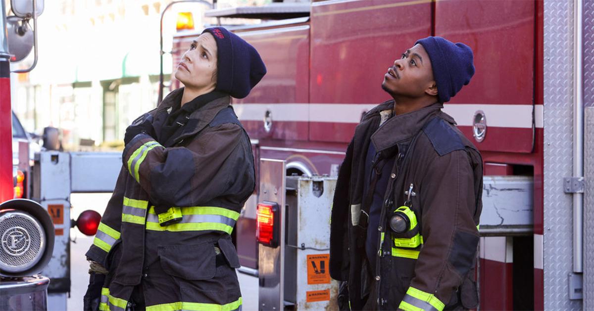 Two firefighters on 'Chicago Fire' looking up surrounded by fire trucks. 