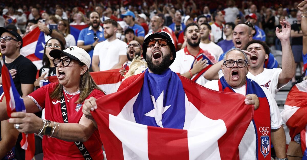 Fans of Puerto Rico cheers sing their country's national anthem, prior to the men's preliminary round group C basketball match between Puerto Rico and Serbia during the Paris 2024 Olympic Games at the Pierre-Mauroy stadium in Villeneuve-d'Ascq, northern France, on July 31, 2024. (Photo by Sameer AL-DOUMY / AFP) (Photo by SAMEER AL-DOUMY/AFP via Getty Images)