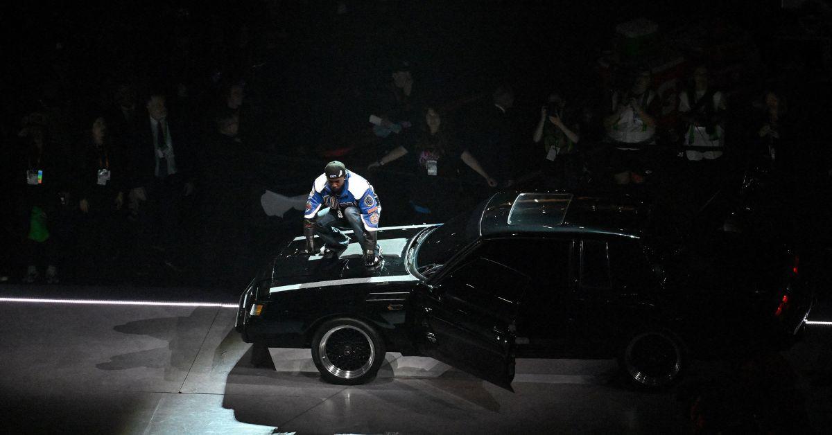 Kendrick Lamar standing on a car at the Super Bowl. 