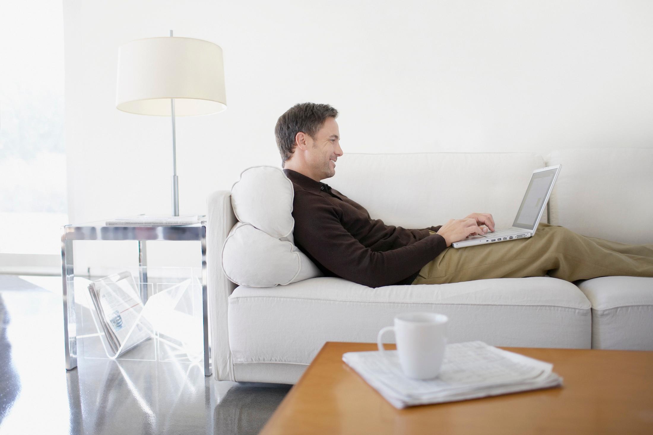 A man relaxing on a sofa and looking on a laptop