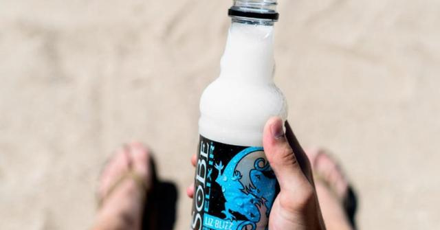 A person holding a white SoBe drink on the beach