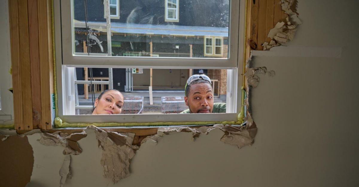 Egypt Sherrod and Mike Jackson peeking through the window of a house under construction