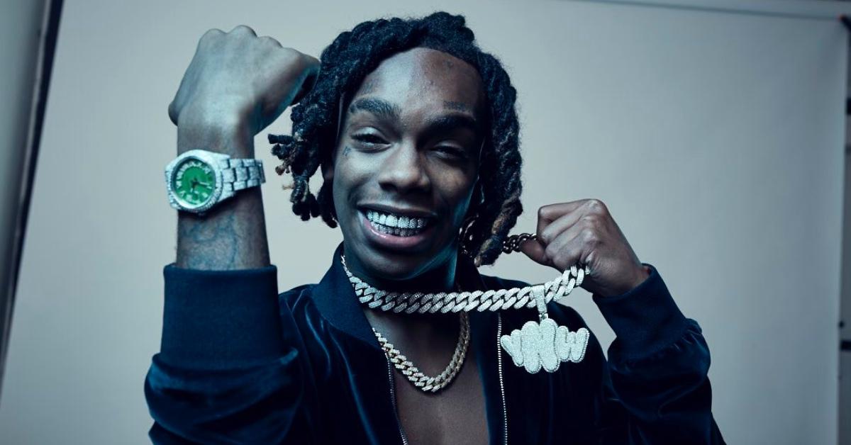 YNW Melly in a blue jacket holding a diamond chain.