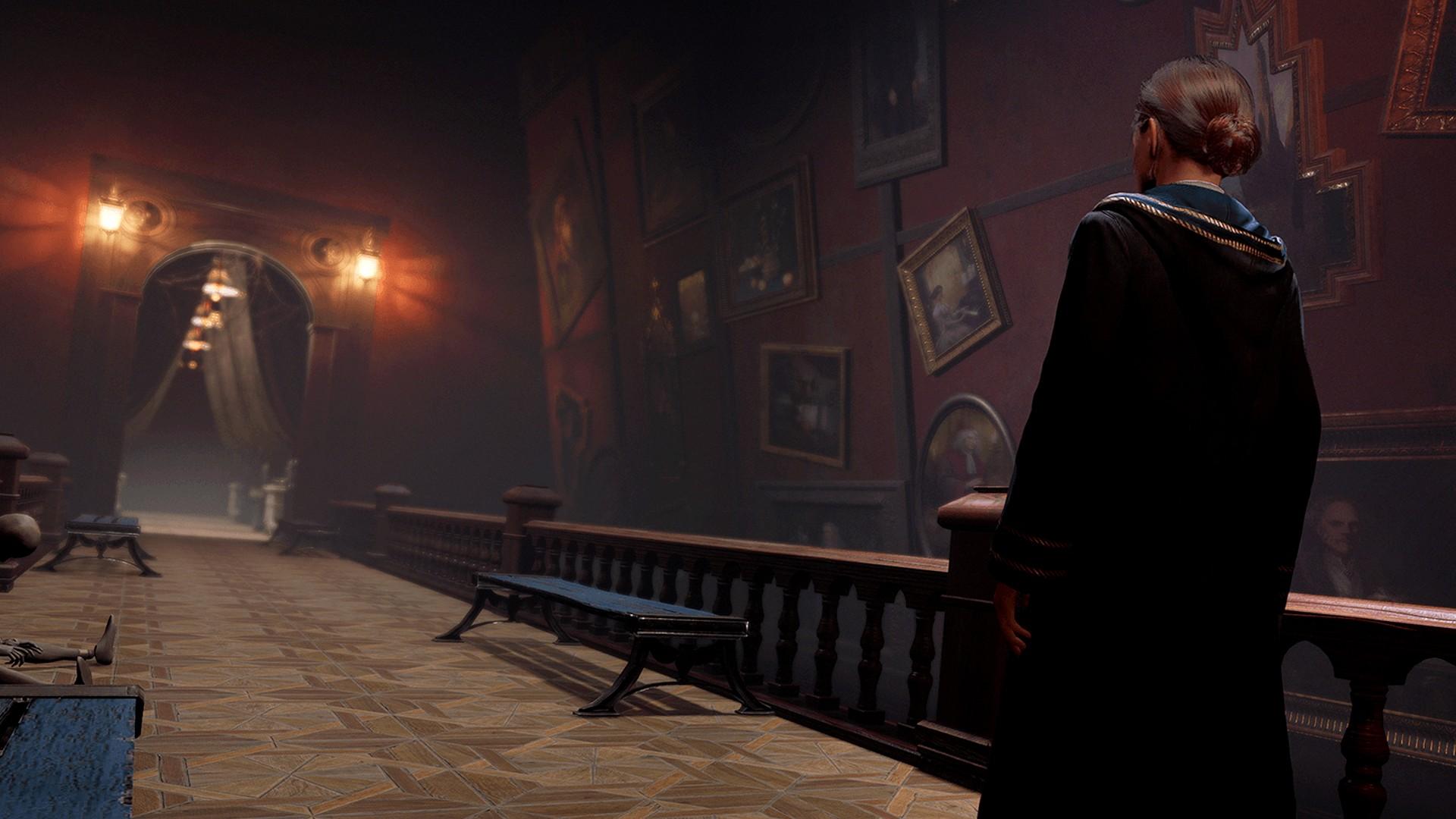 A witch staring down a long winding hallway with paintings in 'Hogwarts Legacy.'