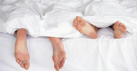 Two people's feet peeking out from under a white comforter.