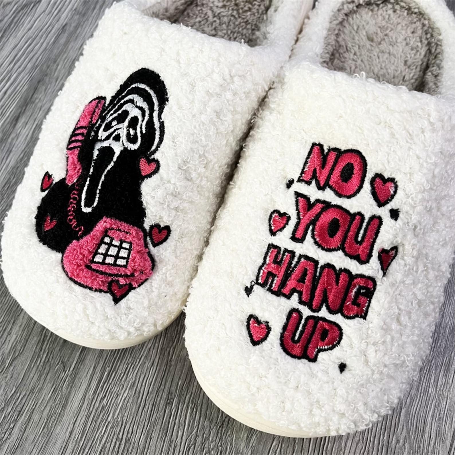 White fuzzy slippers with "no you hang up" and ghostface embroidered on them