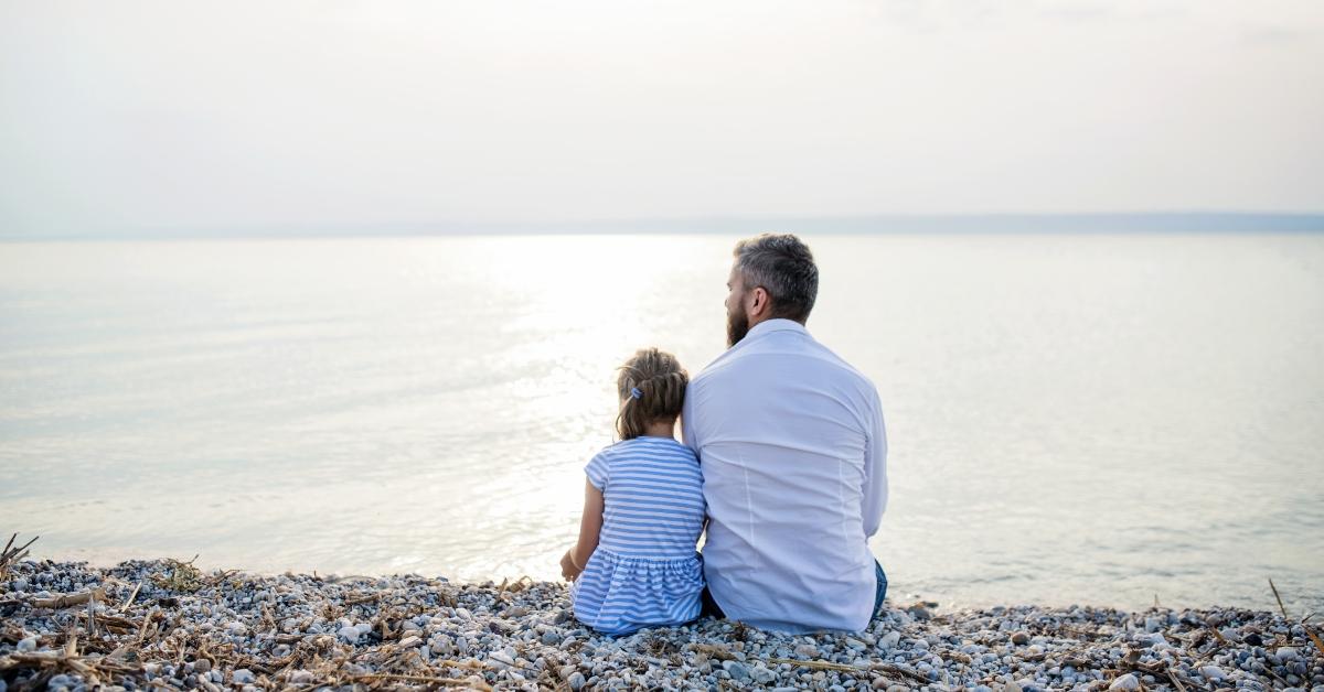 dad and daughter sitting by lake or sea water