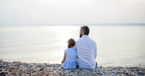 dad and daughter sitting by lake or sea water