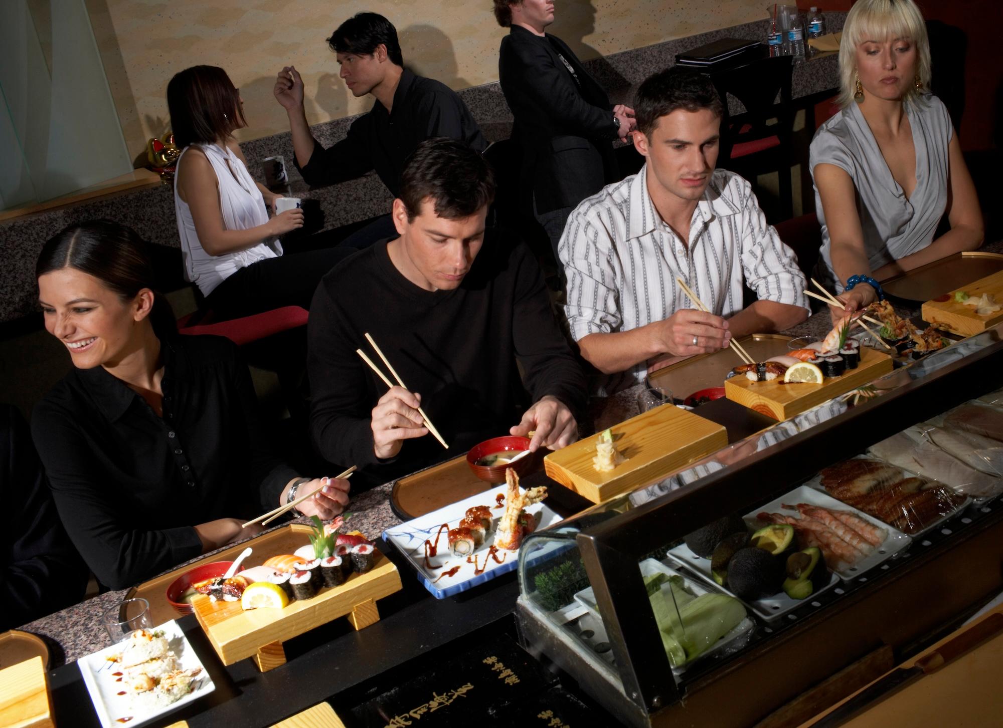 young people eating sushi at the sushi bar counter