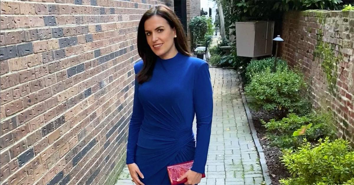 Erin Como in a blue dress standing next to a brick wall. 