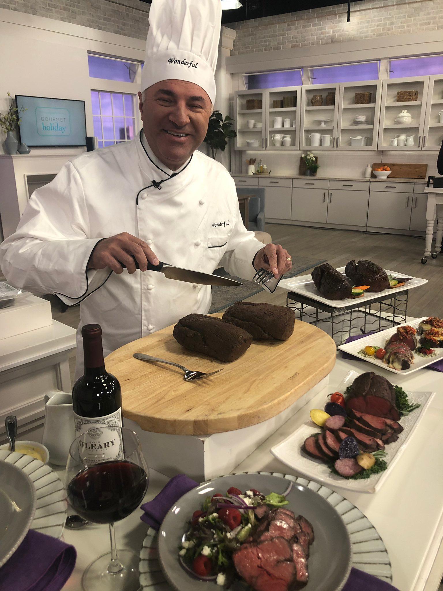 Kevin O'Leary cutting beef wellington while wearing a chef's hat and jacket.