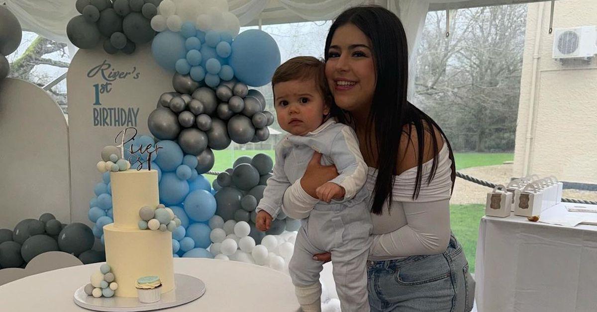 Sophia Grace and her son River on his first birthday in front of balloon backdrop and cake