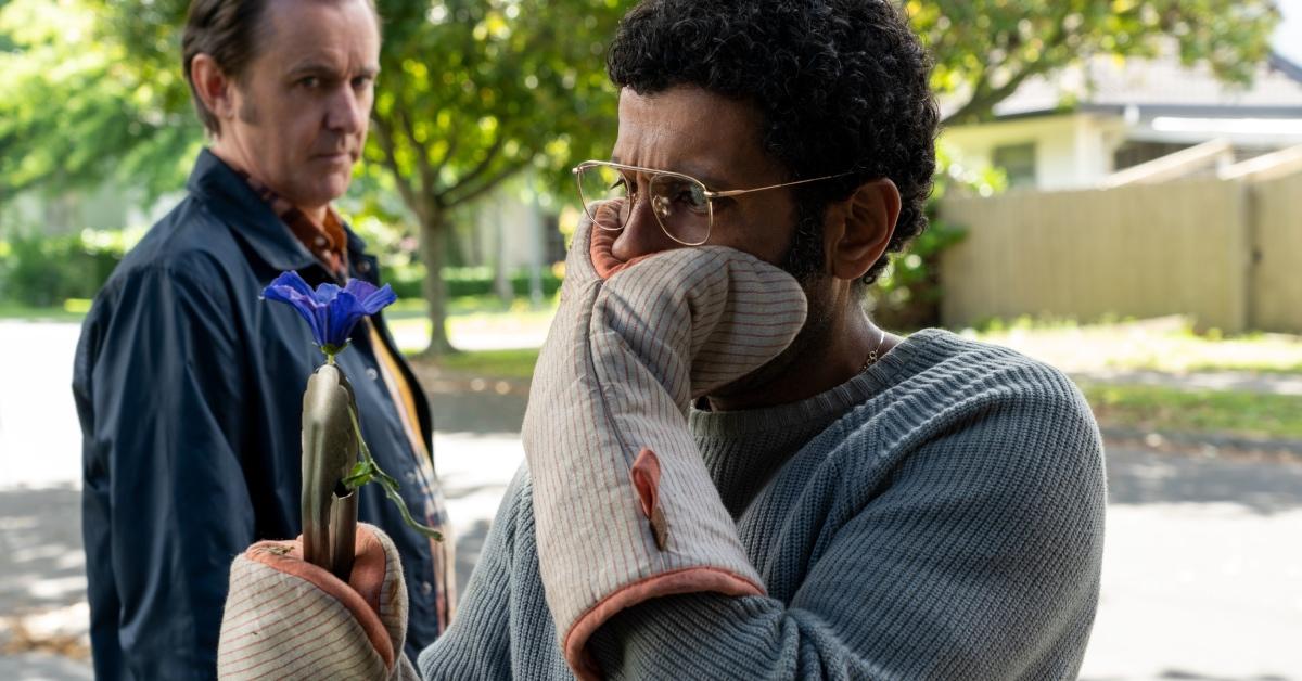 Dr. Singh covering his face while holding a purple flower.