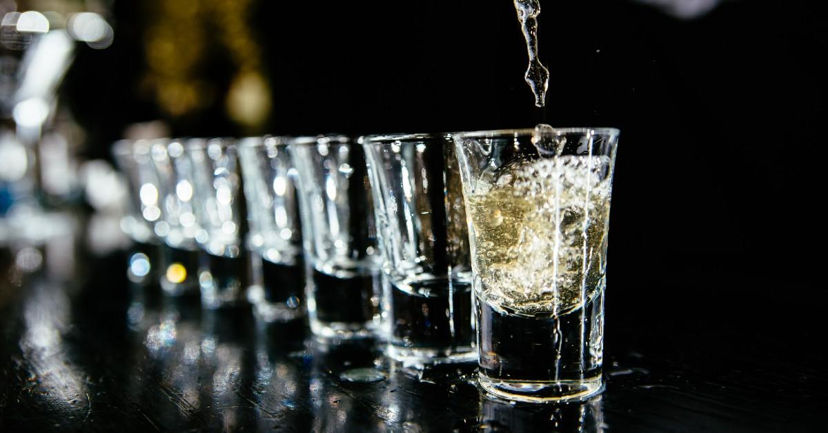 A line of shot glasses being filled atop a black bar