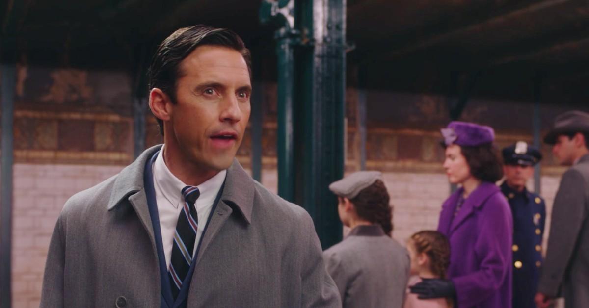 Sylvio (Milo Ventimiglia) looks annoyed at the New York subway in a gray suit and blue tie 