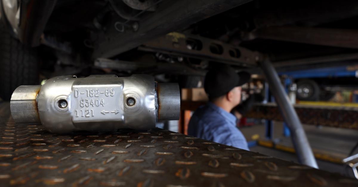 A brand new catalytic converter sits on a car lift.