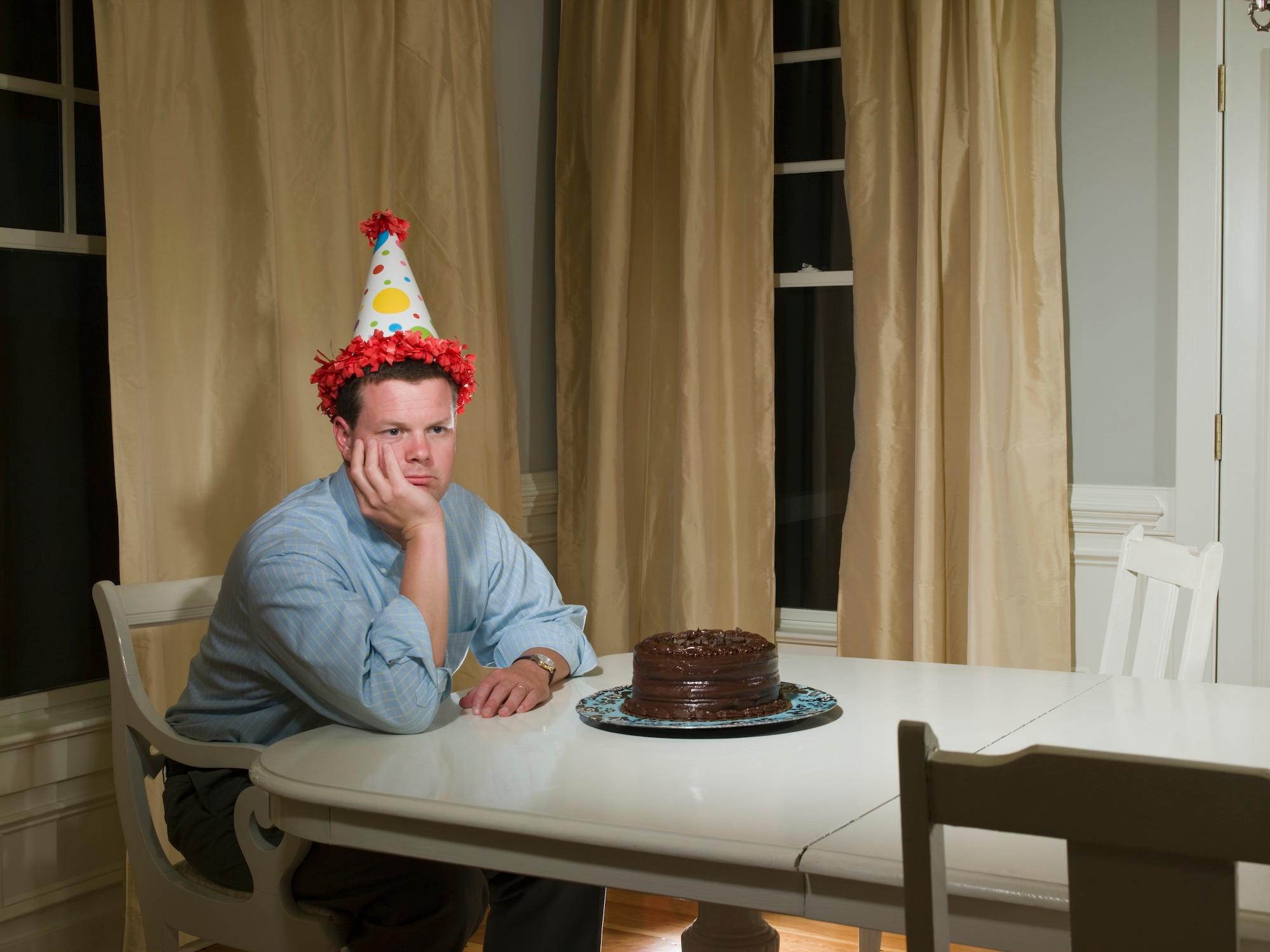 Mid adult man in party hat, sitting at table in front of birthday cake