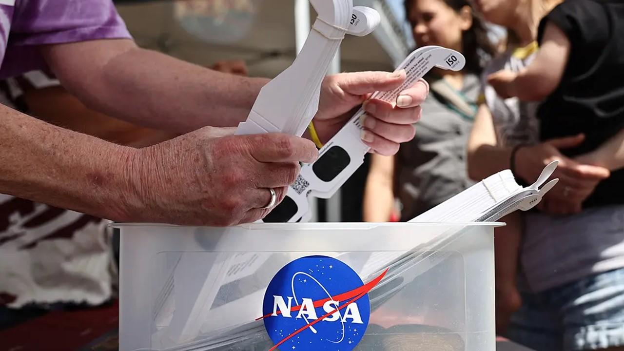 A person holding solar eclipse glasses from NASA