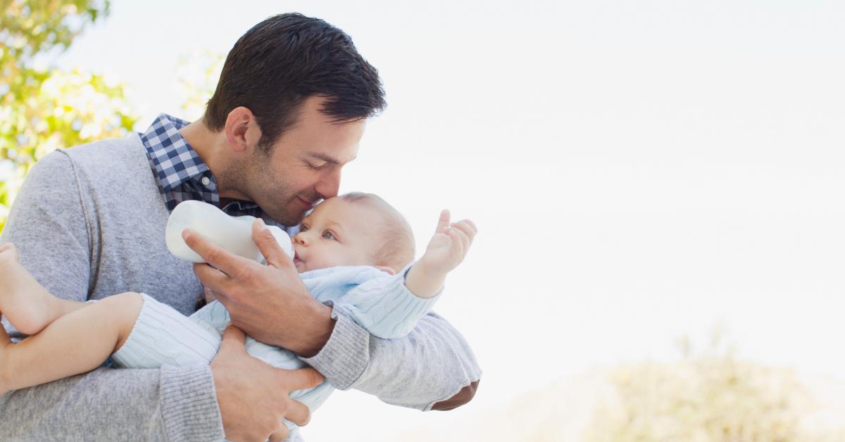 A dad bottle feeds his baby outside.