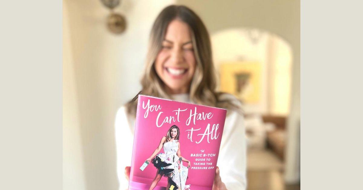 Stassi Schroeder holds up a copy of her book "You Can't Have It All: A Basic B*tch Guider to Taking the Pressures Off'