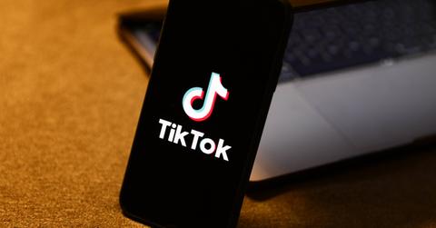 The TikTok logo on a phone leaning on a laptop.