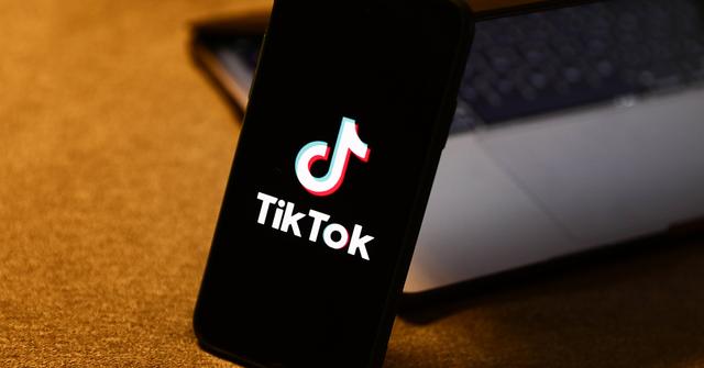 The TikTok logo on a phone leaning on a laptop.