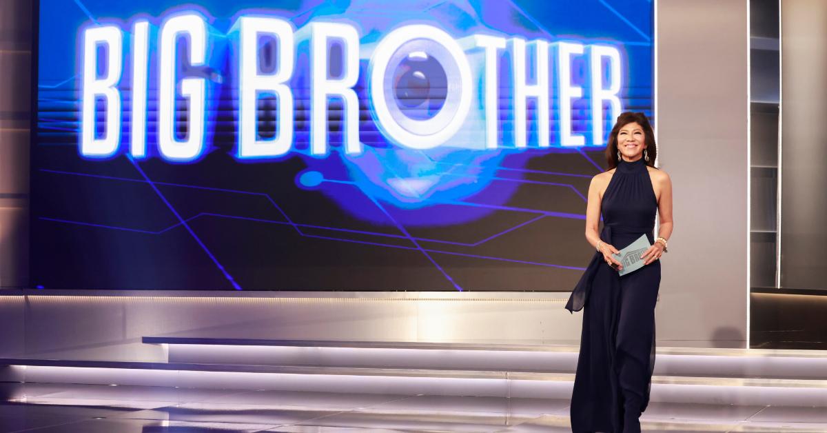 Julie Chen Moonves wears a black high-neck gown and smiles on stage with the 'Big Brother 26' logo behind her.