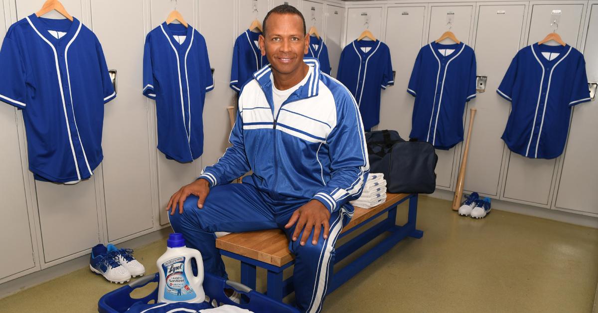 Alex Rodriguez poses in a locker room, wearing a blue and white tracksuit. Lysol Laundry Sanitizer sits in a laundry basket at his feet.