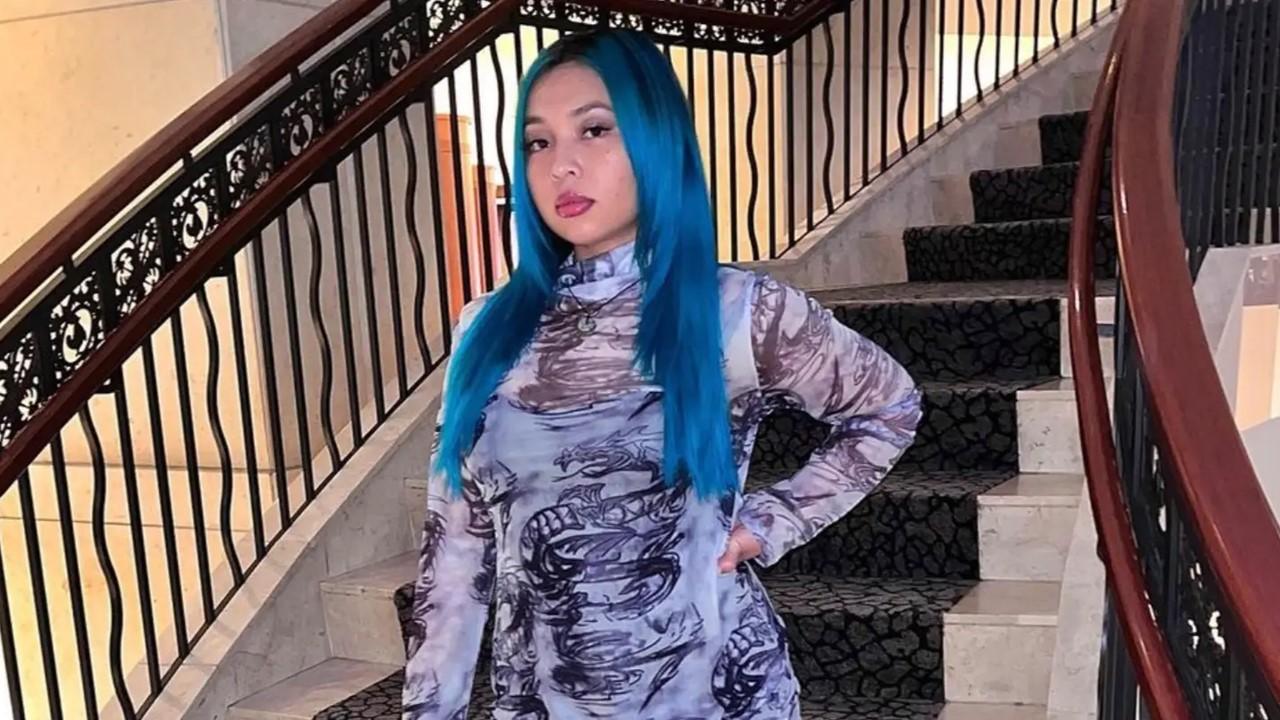 Chau standing in front of a staircase with blue hair