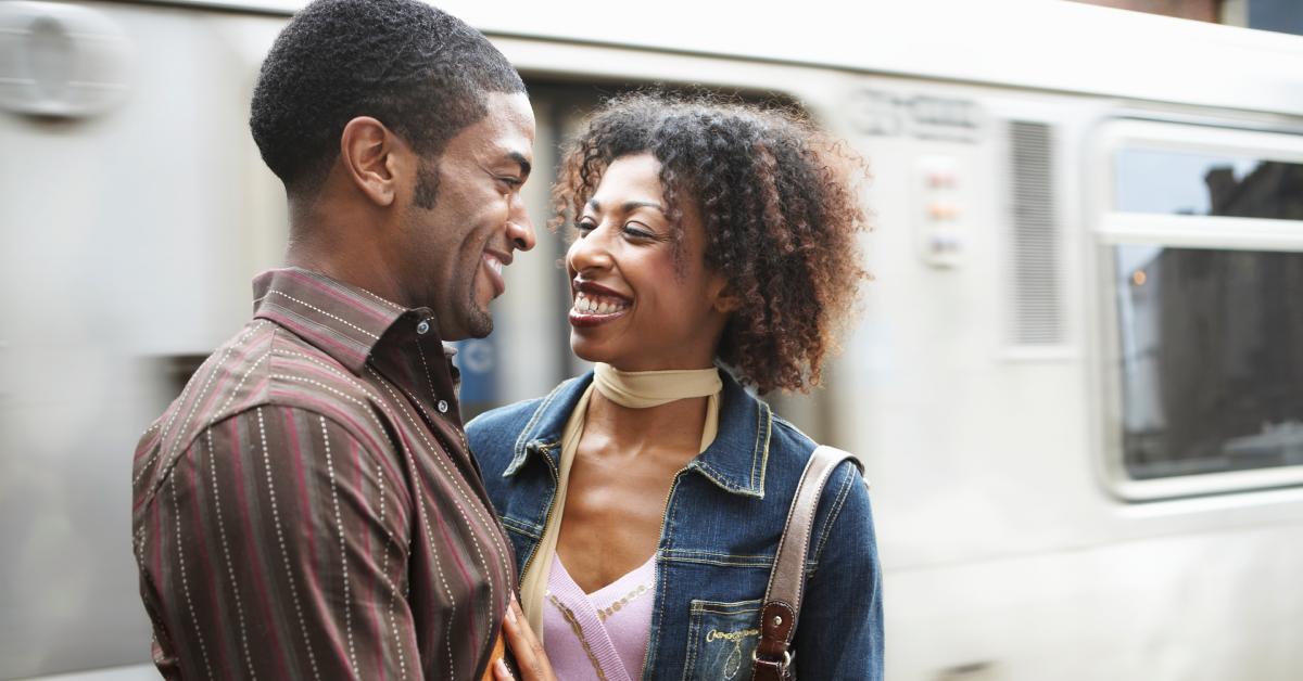 A young couple smiles at each other while waiting on the train platform.