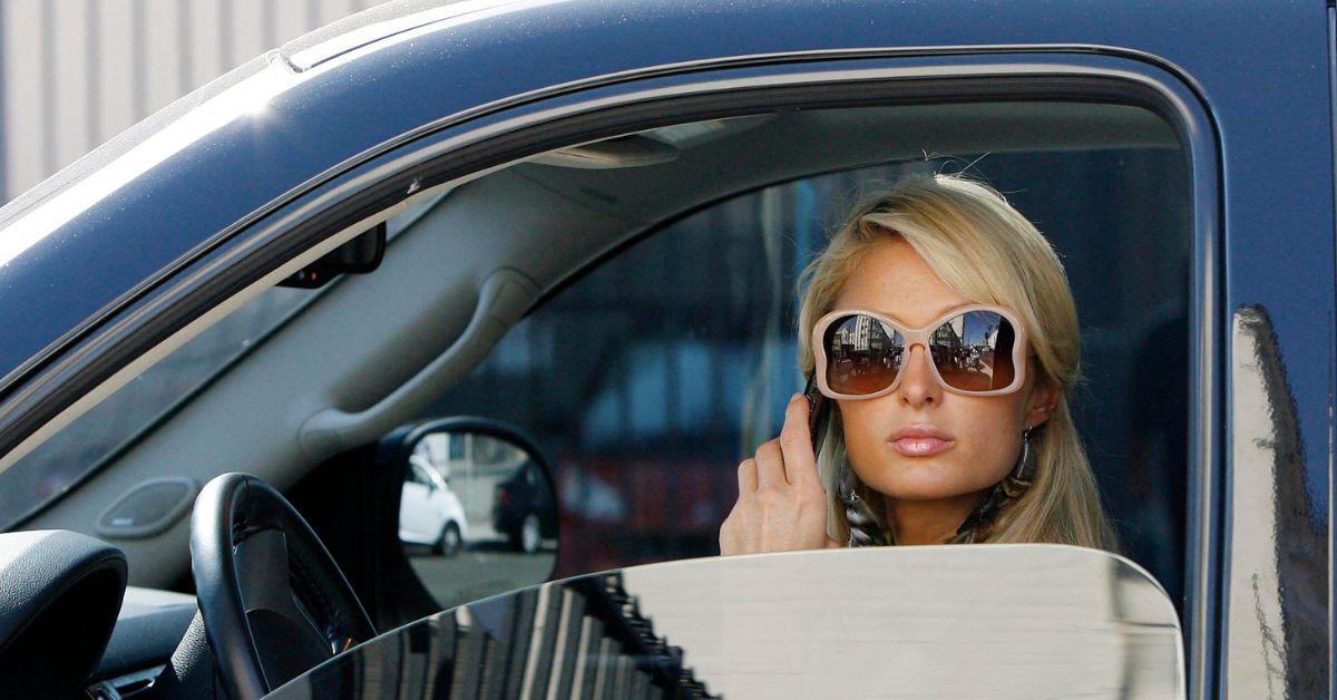 Paris Hilton on the phone in a car wearing sunglasses. 