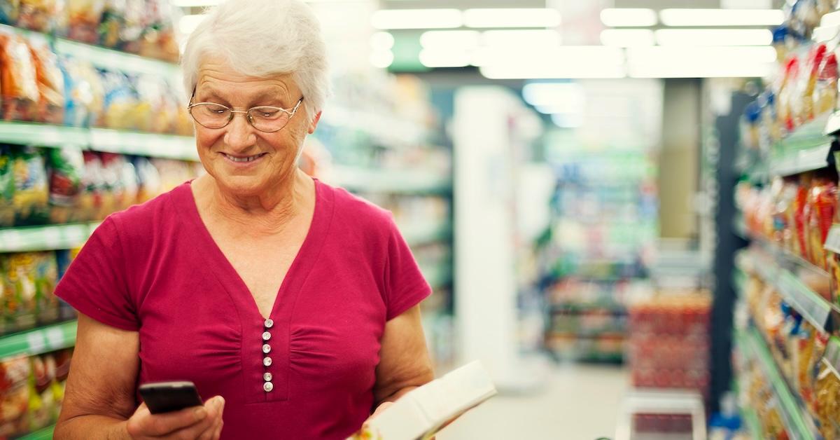 An elderly woman looking at her phone in the grocery store