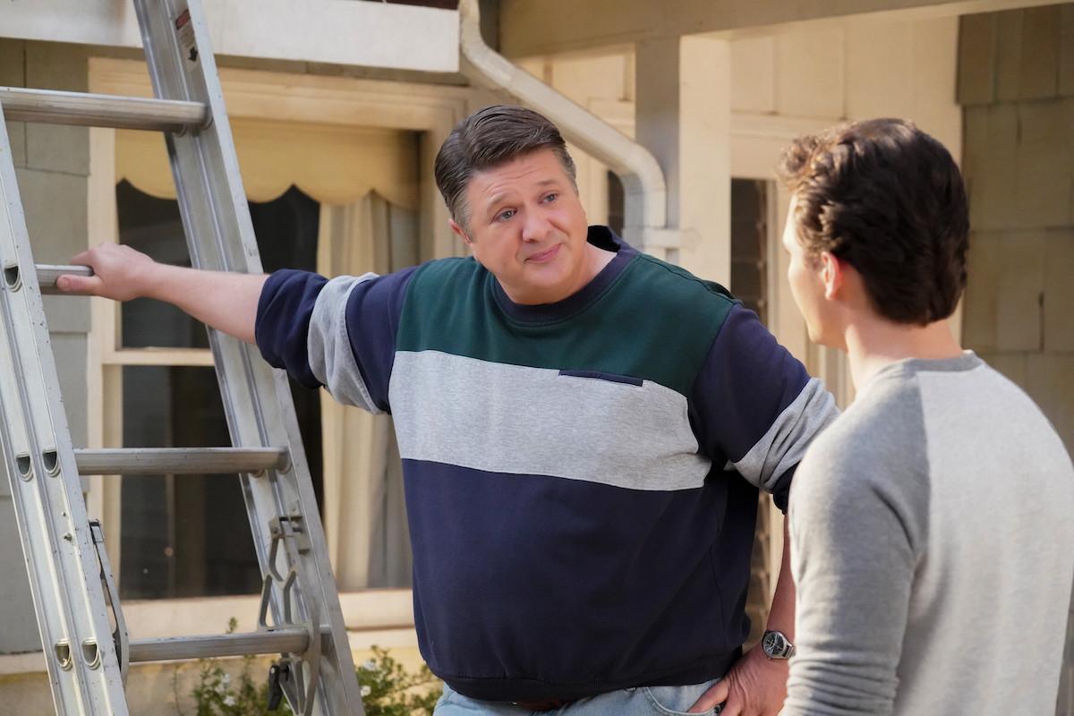 George wears green and white sweater and stands in front of a ladder on 'Young Sheldon'.