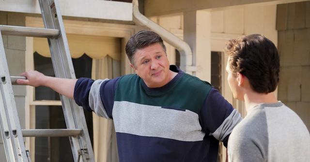 George wears green and white sweater and stands in front of a ladder on 'Young Sheldon'.