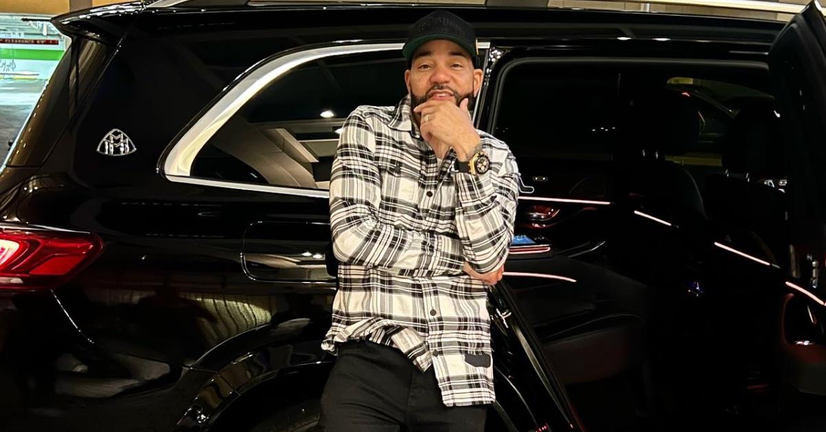 DJ Envy posing next to a black SUV.