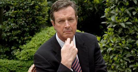 Michael Crichton with his hand on his chin in a garden.