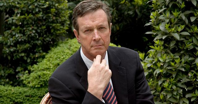 Michael Crichton with his hand on his chin in a garden.