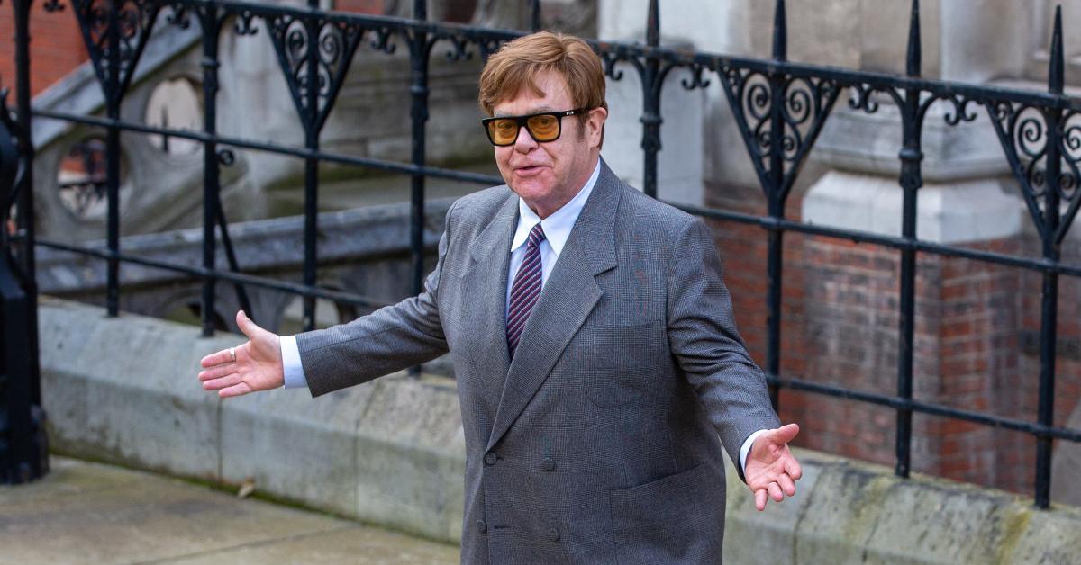 Elton John standing outside with a suit on.