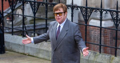 Elton John standing outside with a suit on.