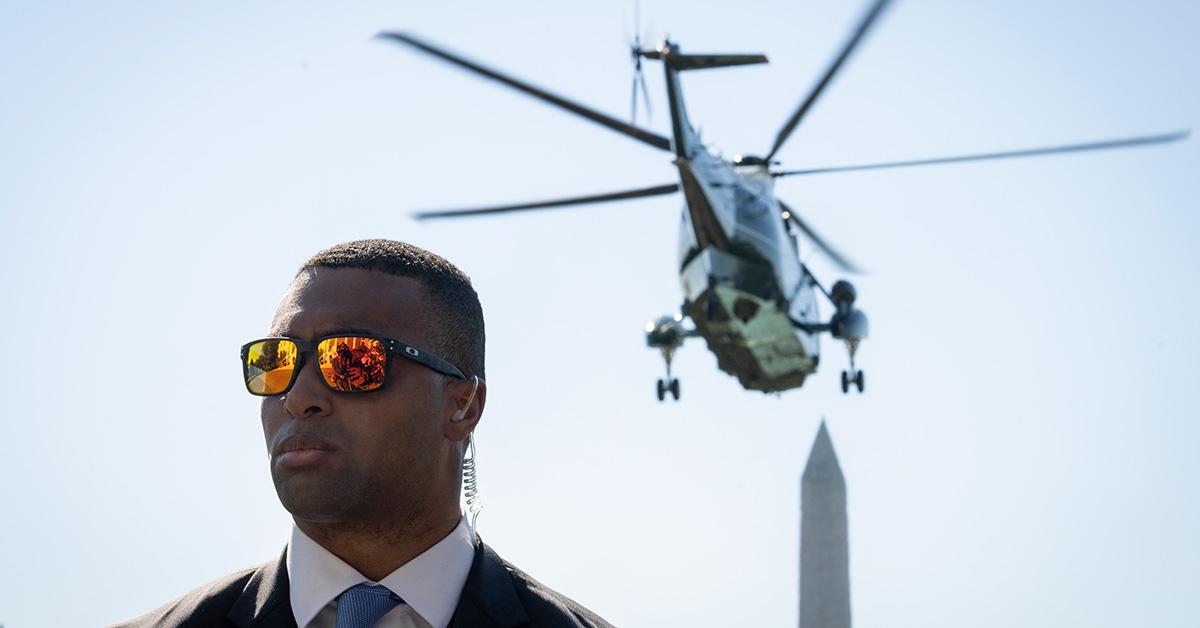 A Secret Service agent wearing sunglasses as Joe Biden departs on a helicopter. 