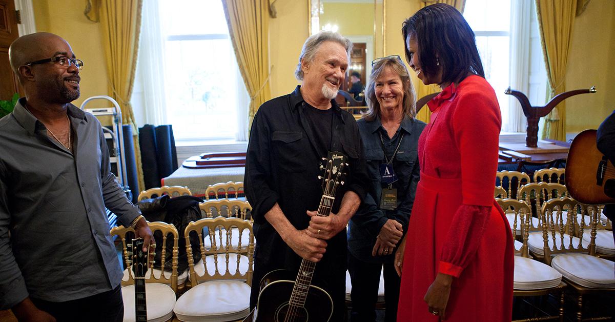 Kris Kristofferson holding a guitar speaking with Michelle Obama. 