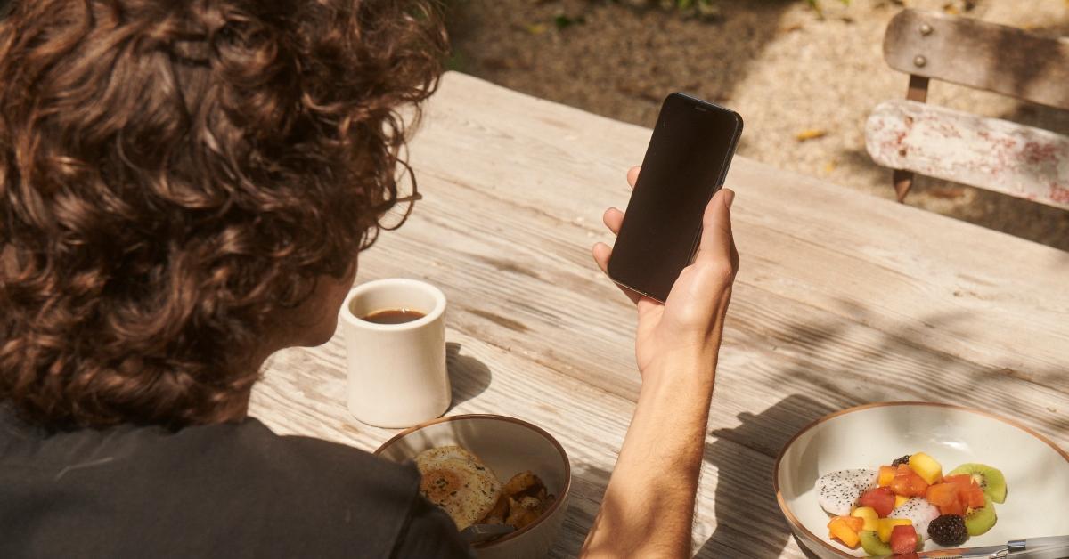 person looking at phone while eating breakfast