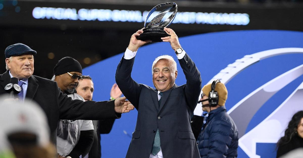 Jeffrey Lurie holding up the 2025 NFC East championship trophy