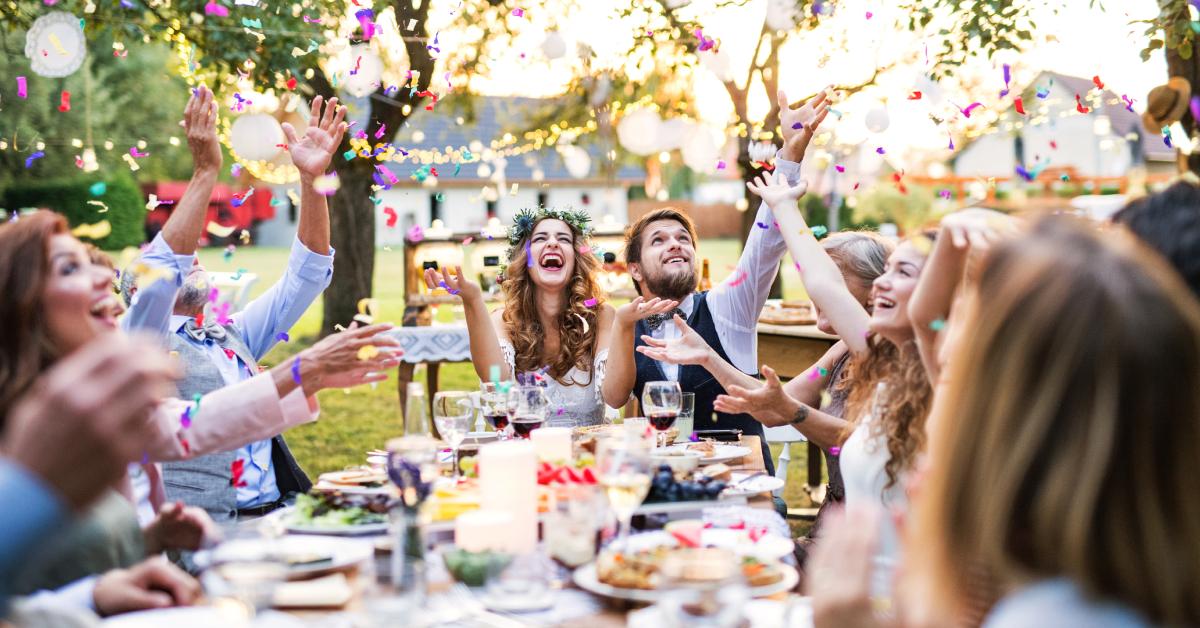 A bride and groom with many guests at their outdoor wedding reception.