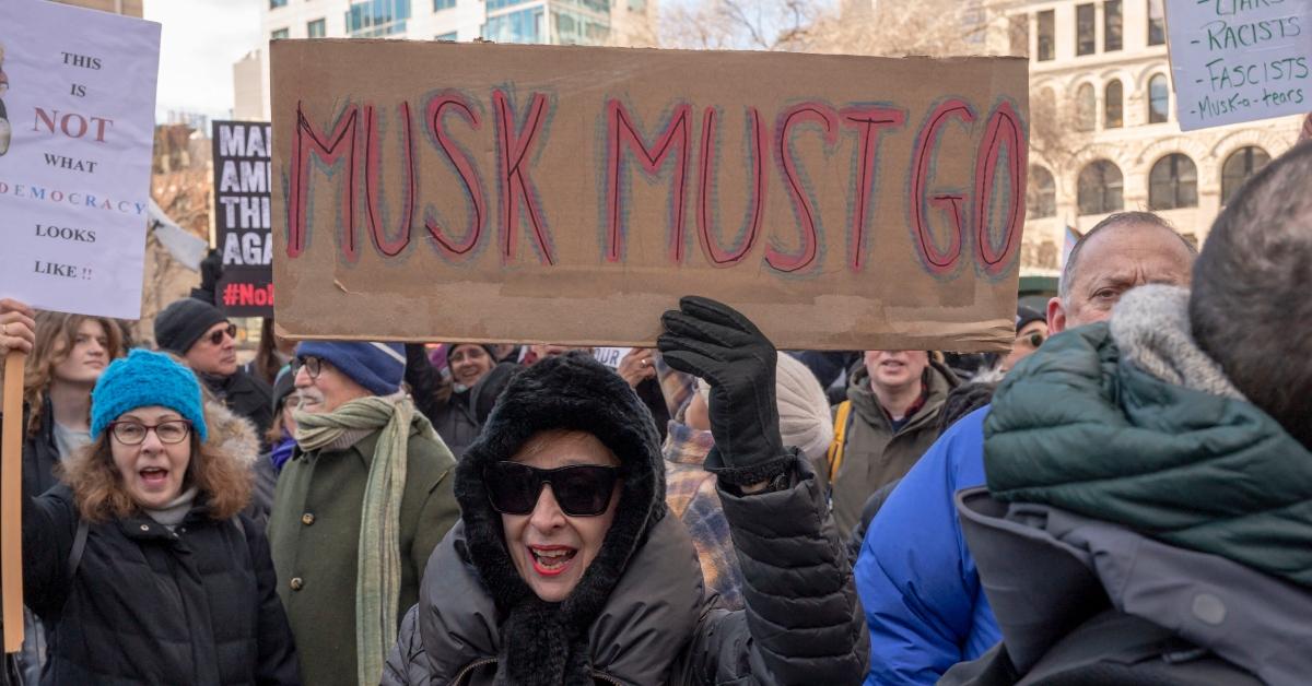 A protest sign reads "Musk Must Go"