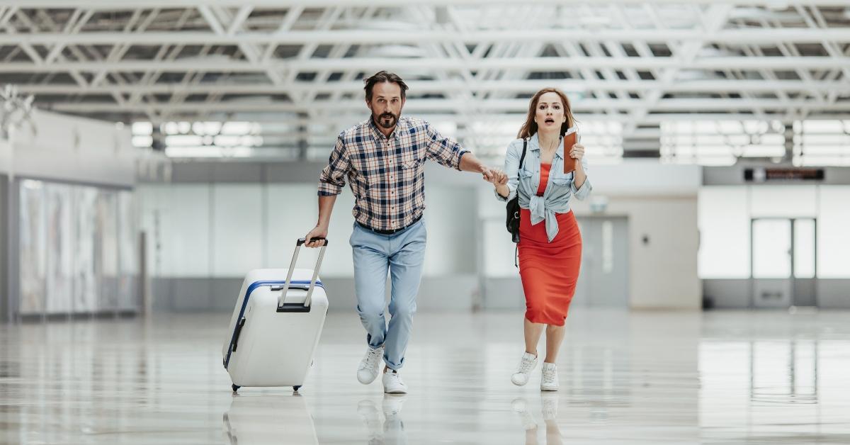 Full length portrait of worried male and woman running through the airport with baggage.